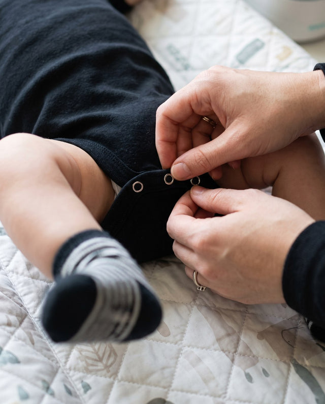 Manos cerrando los broches del body negro en un cambio de pañal