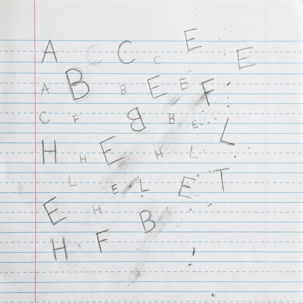 Hoja de práctica con letras de tamaños dispares, fuera de las líneas y con tachones